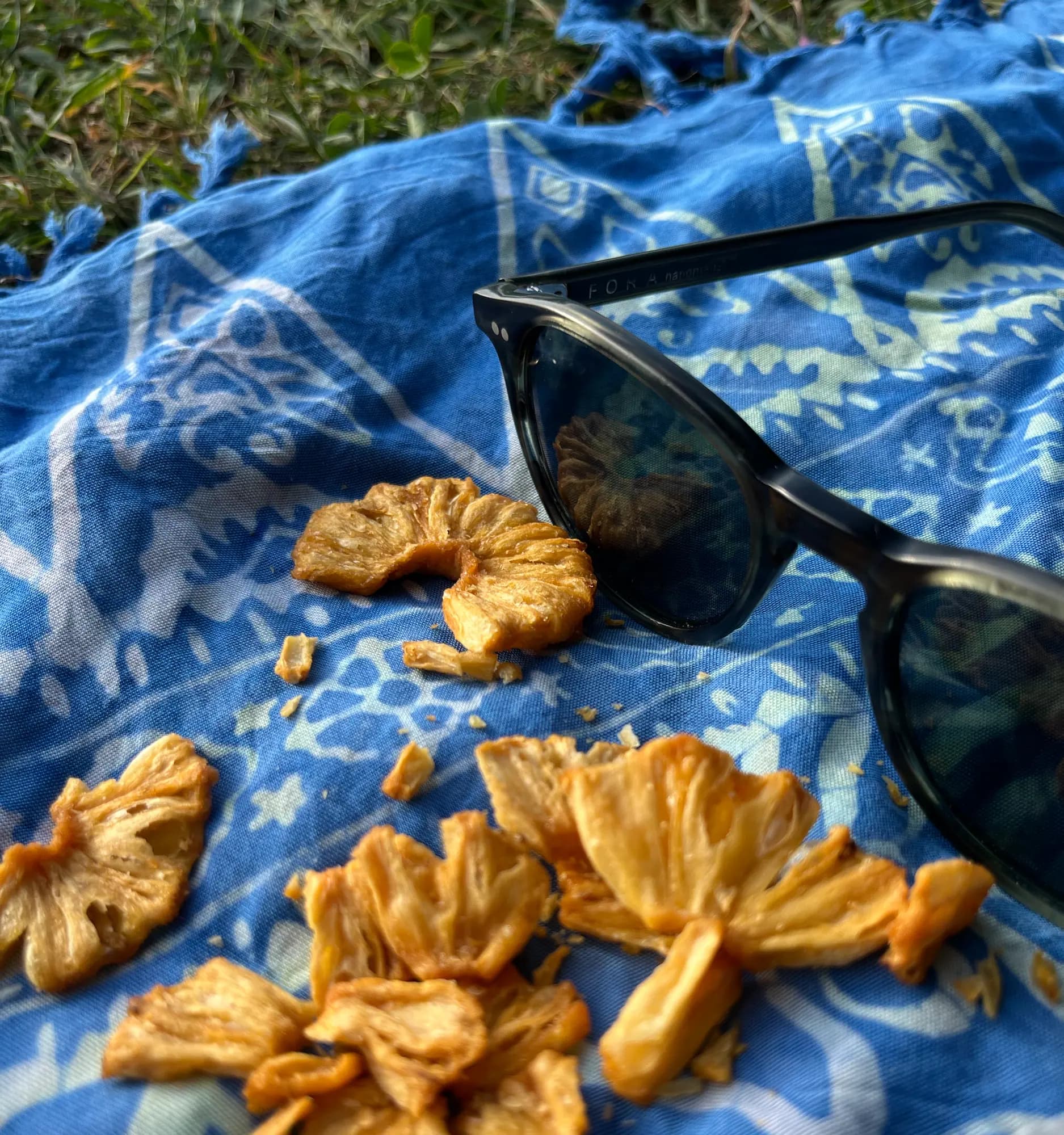 Close-up of golden Crispy Ananas pieces on a blue picnic blanket next to a pair of sunglasses