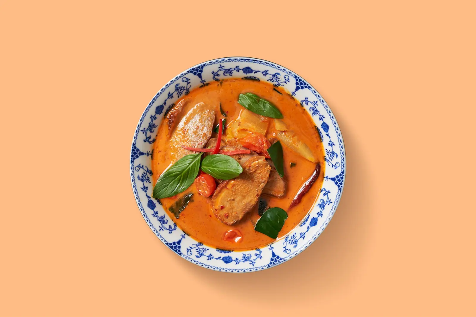 Entencurry mit Ananas in einer blau-weissen Schale, orangefarbener Grund